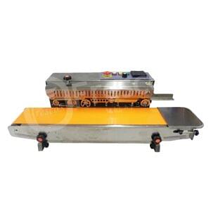 The Auto Sealing Machine Stainless Steel Premium FR770 features a stainless steel build with an orange conveyor belt and top-mounted control buttons and power switch, representing advanced auto sealing technology.