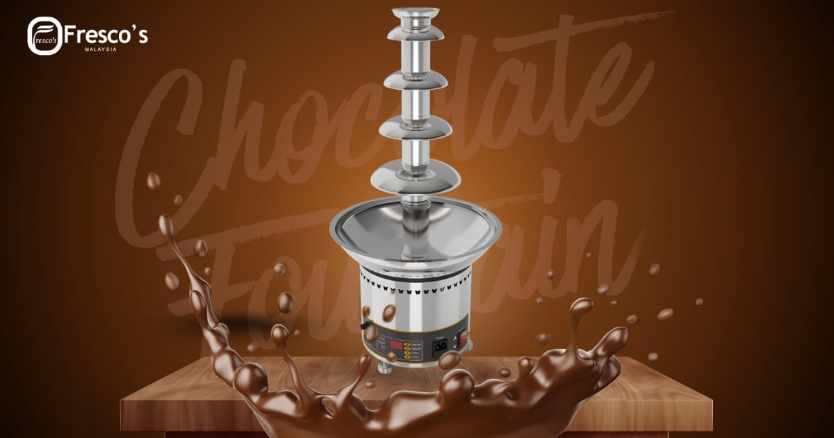 A stainless steel chocolate fountain on a brown surface with chocolate splashing around, a waffle stick maker nearby, and the Fresco's logo in the top left corner.